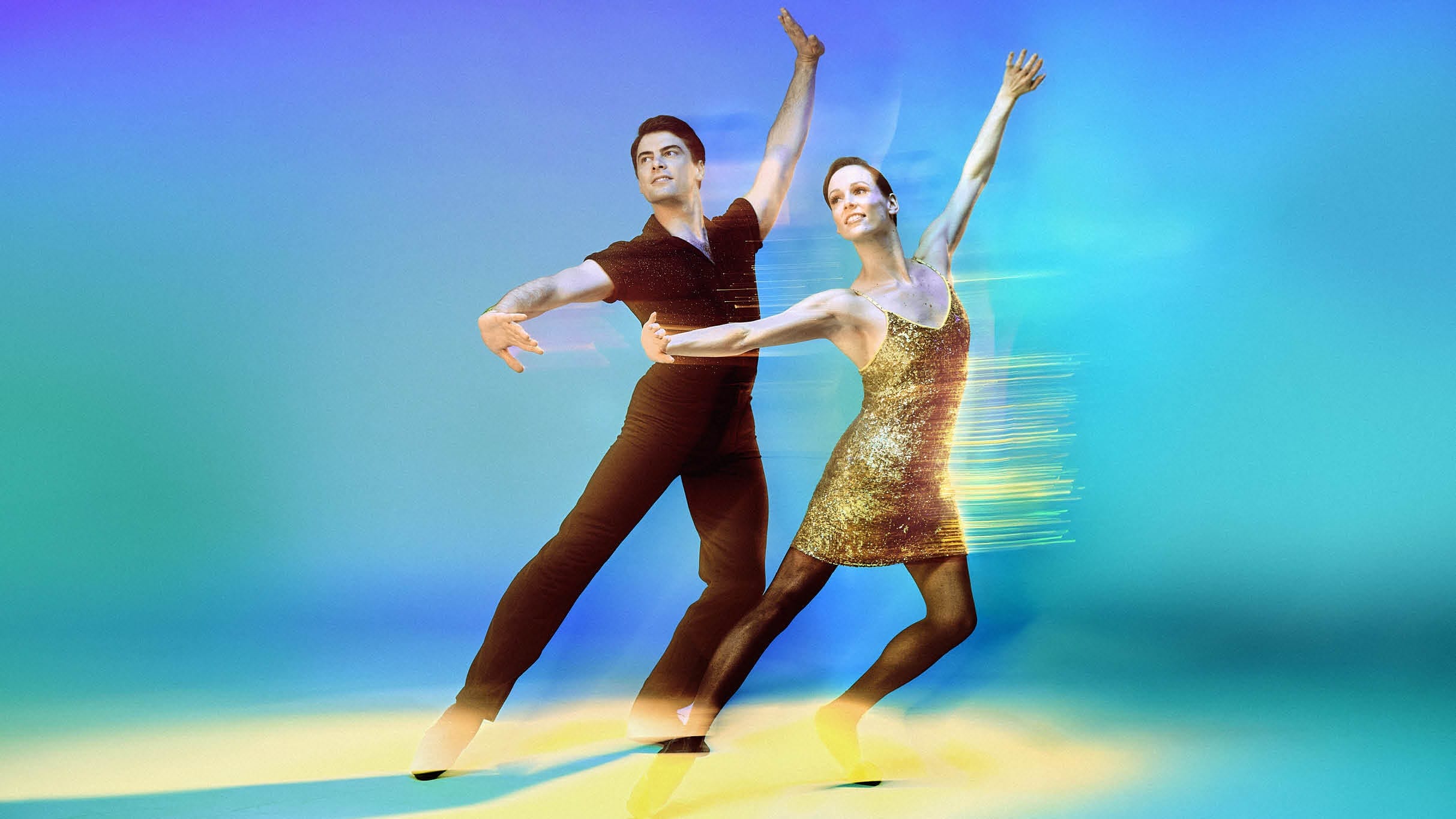 Two ballet dancers pose gracefully against a colorful, blurred background, with the female dancer in a gold dress and the male dancer in black attire.