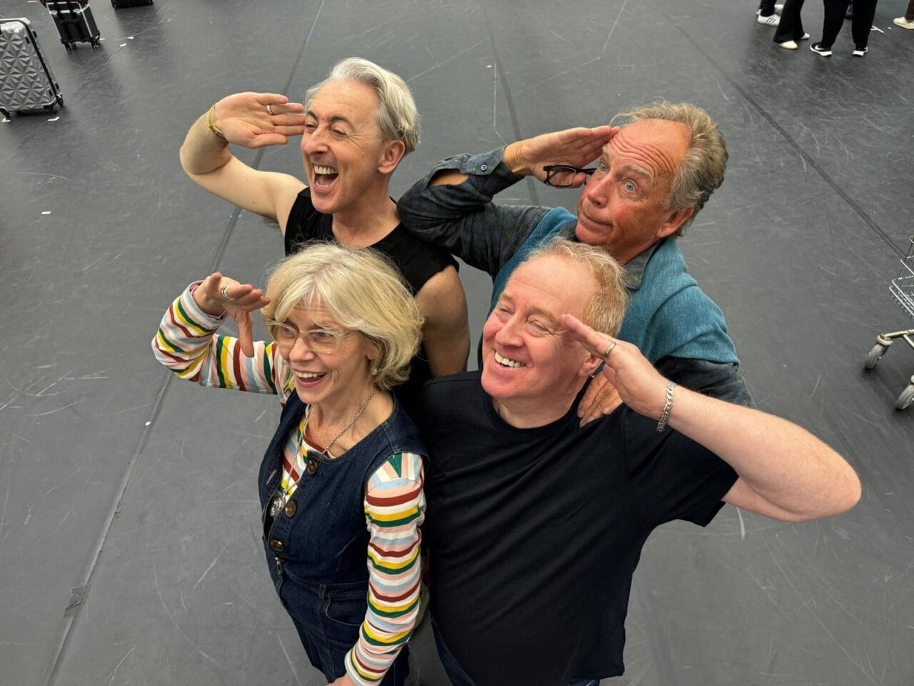 Four adults stand in a staggered formation indoors at Festival Theatre, all smiling and giving a salute gesture while looking upwards, embodying the spirit of the High Life.