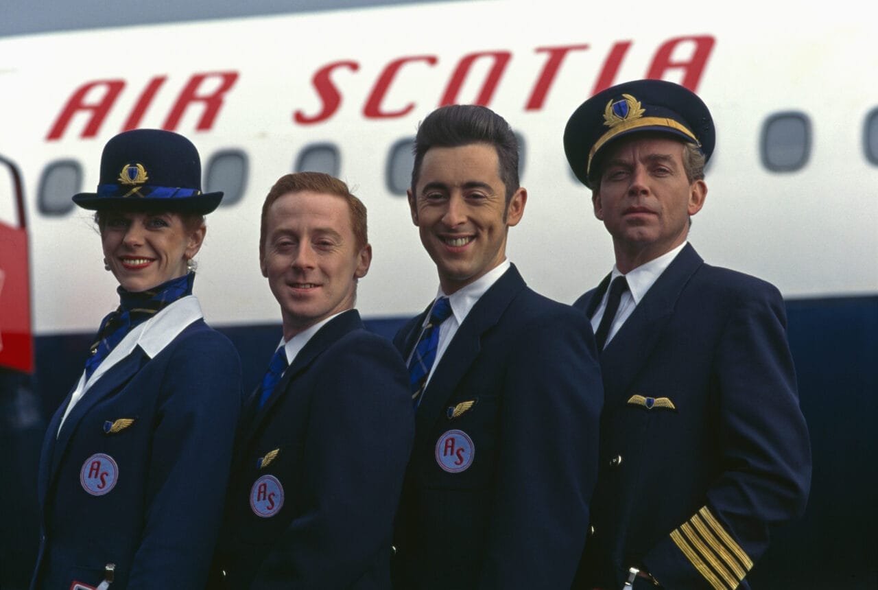 Four airline crew members in uniform stand in front of an airplane with "Air Scotia" visible on the side, ready to bring the High Life to travelers heading to their next adventure.