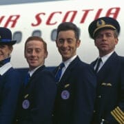 Four airline crew members in uniform stand in front of an airplane with "Air Scotia" visible on the side, ready to bring the High Life to travelers heading to their next adventure.