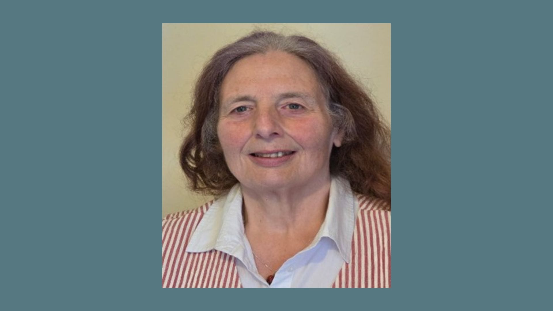 A woman with long brown hair, wearing a white collared shirt and a striped vest, is smiling at the camera against a neutral background—introducing Cllr Margaret Graham from the Capital Theatres Board.