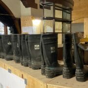 A row of black rubber boots is lined up on a wooden counter in a room under construction or renovation, with office supplies and blueprints visible in the background.