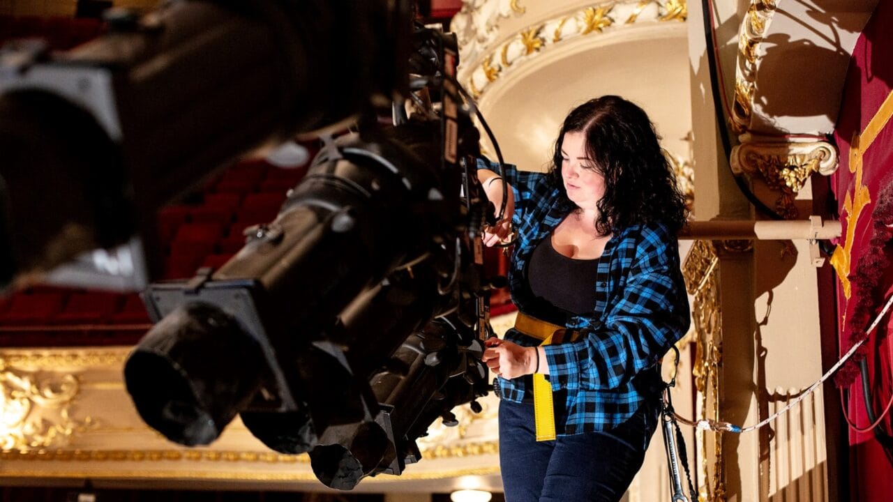 A person adjusting stage lighting equipment on a platform inside an ornate theater.