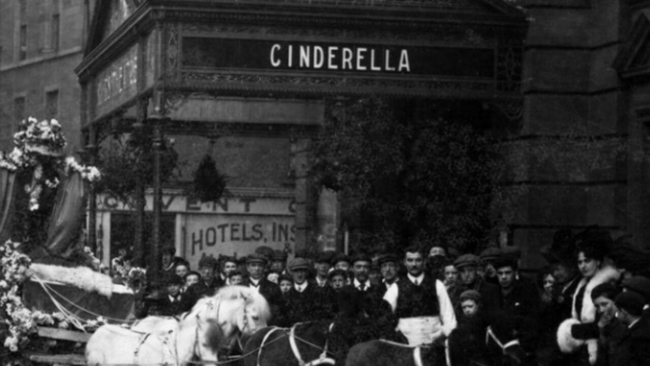 A crowd gathers outside a theater showing "Cinderella"; a horse-drawn carriage is in front of the building.