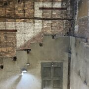 Interior view of a partially renovated brick wall with exposed areas, an old door, a large open window, and visible construction materials.