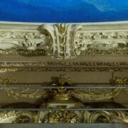 Ornate architectural ceiling with intricate moldings and gold accents, partially obscured by metal scaffolding.