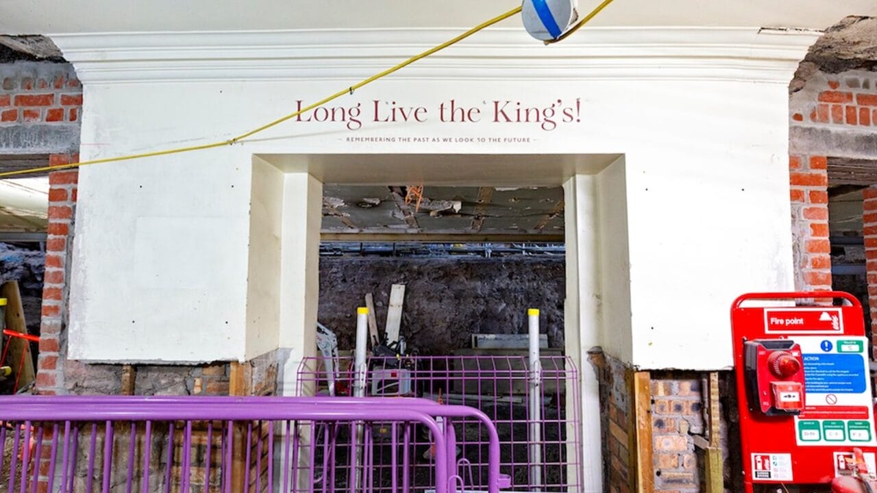 A partially demolished building interior with a sign reading "Long Live the Kings!" above a blocked doorway, construction barriers, and a red fire alarm box on the right.