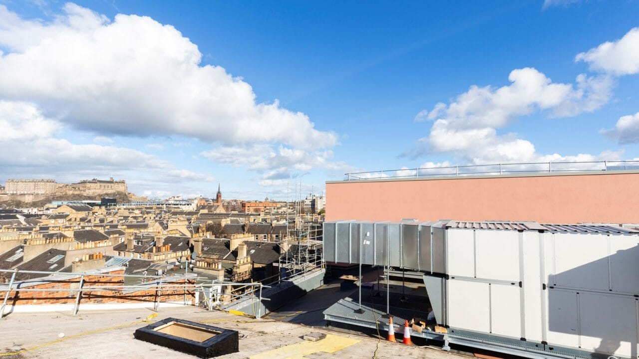 Rooftop view of a city, scaffolding, and Edinburgh Castle in the background.