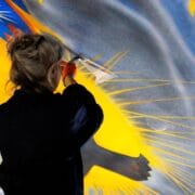 A person in gloves restores a colorful ceiling mural, using a small tool to clean or repair the painted surface.