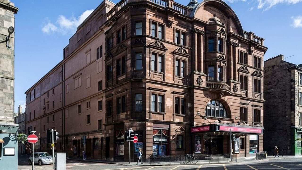 Historic red-brick theatre building on a street corner with arched windows, ornate architectural details, and a covered entrance.
