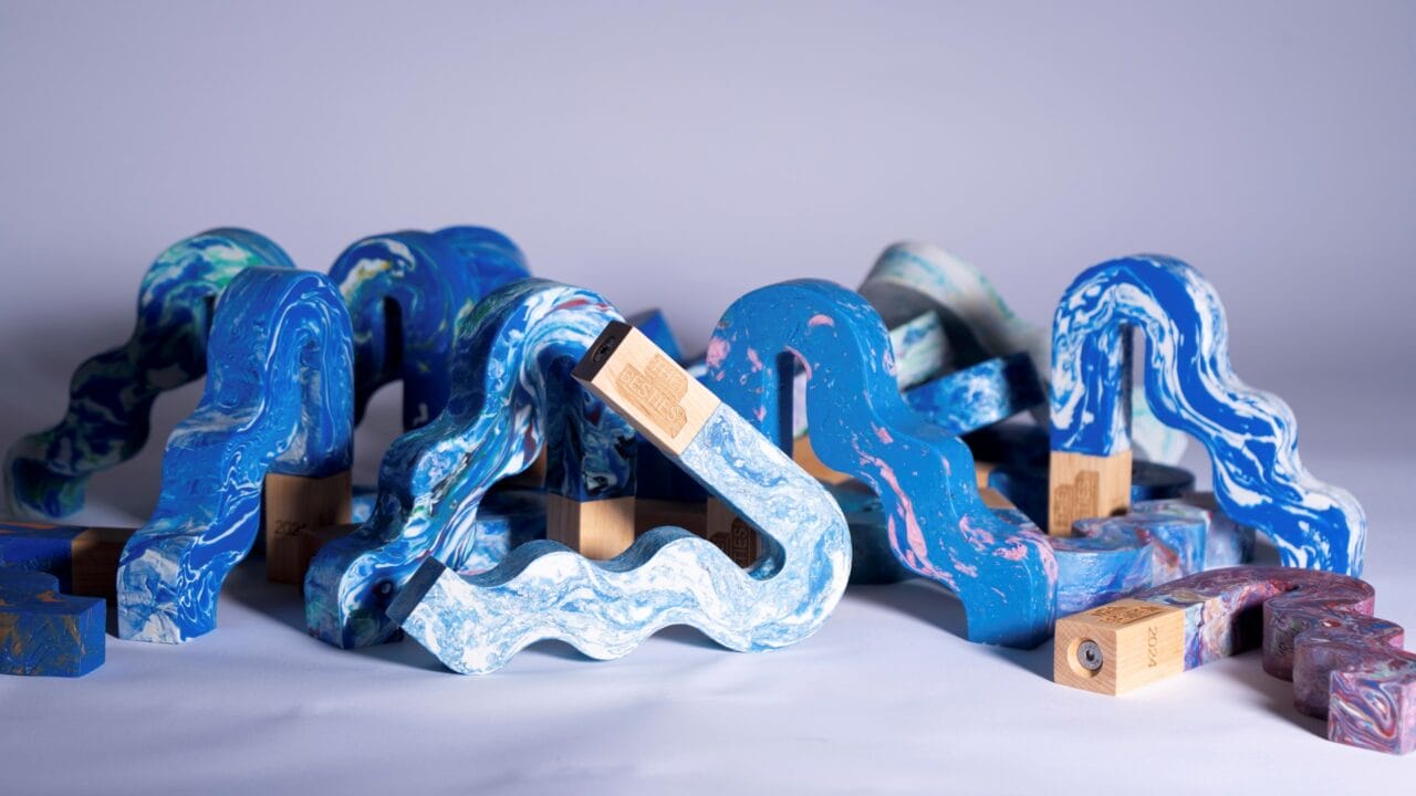 Several wavy, multicoloured objects with marbled patterns and wooden bases are arranged on a light surface against a plain background.