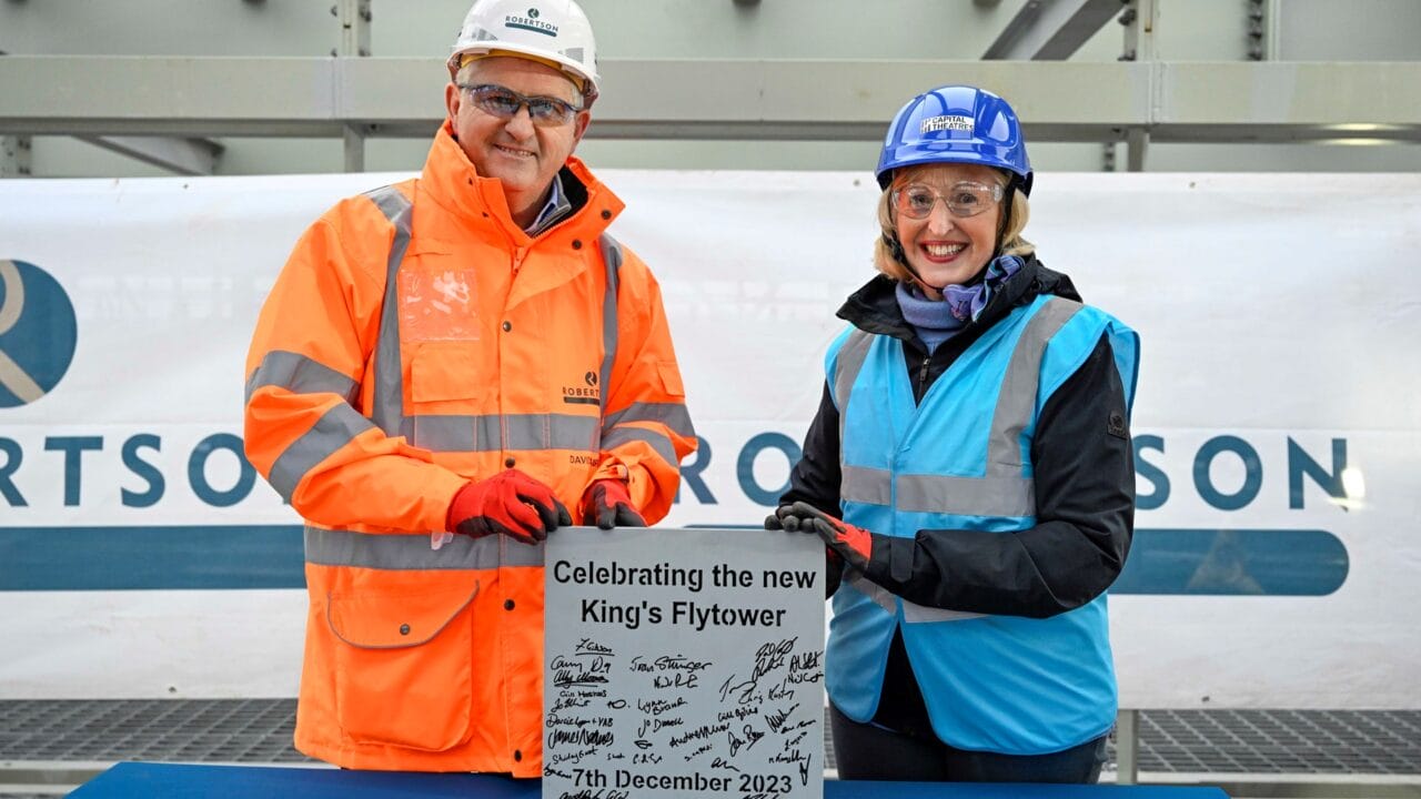 Two people in safety gear stand beside a commemorative plaque signed by others, marking the celebration of the new King's Flytower, dated 7th December 2023.
