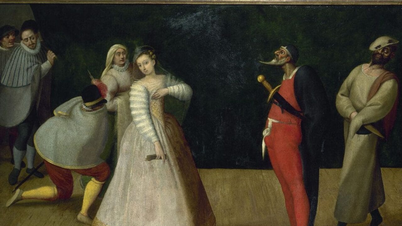 A group of people in historical costumes, including masked figures, gather on a wooden stage with a dark backdrop.