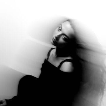 Black and white photo of a woman in a dark outfit with blurred motion, sitting against a light background, her long hair flowing to the side.