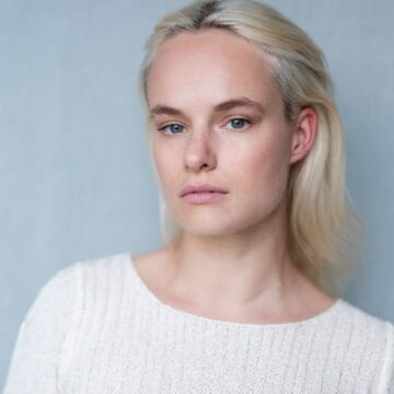 Emma Evelein, a woman with light blonde hair and blue eyes, poses in a cream-colored textured top against a plain light grey background.