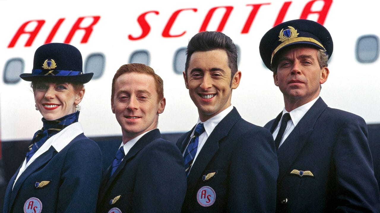 Four airline crew members in uniform stand in front of an airplane with "Air Scotia" written on it, smiling at the camera and embodying the spirit of the High Life.