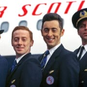 Four airline crew members in uniform stand in front of an airplane with "Air Scotia" written on it, smiling at the camera and embodying the spirit of the High Life.