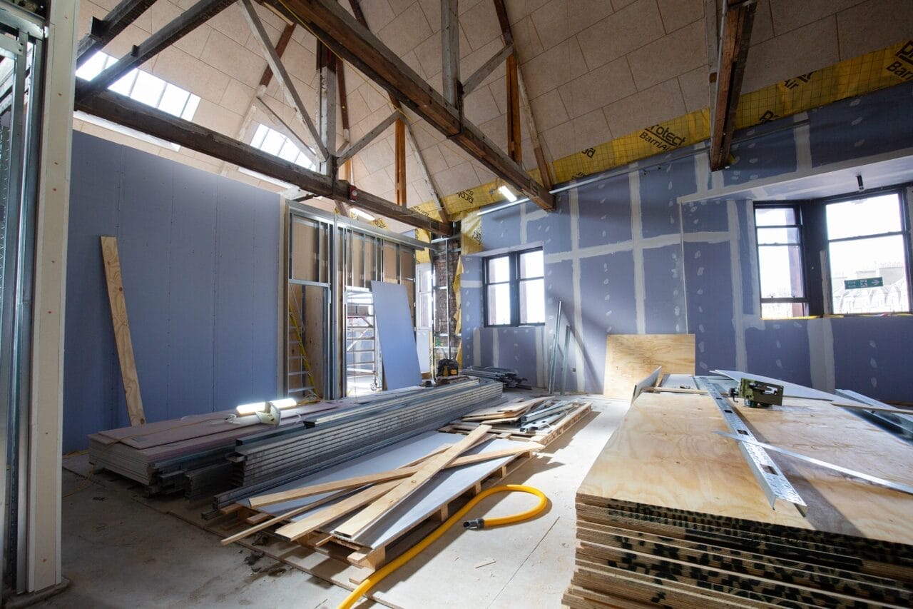 Interior of the Creative Engagement space in the King's Theatre showing exposed beams, drywall sheets, plywood, ladders, tools, and construction materials scattered on the floor. The new partition walls are highlighted in this image.