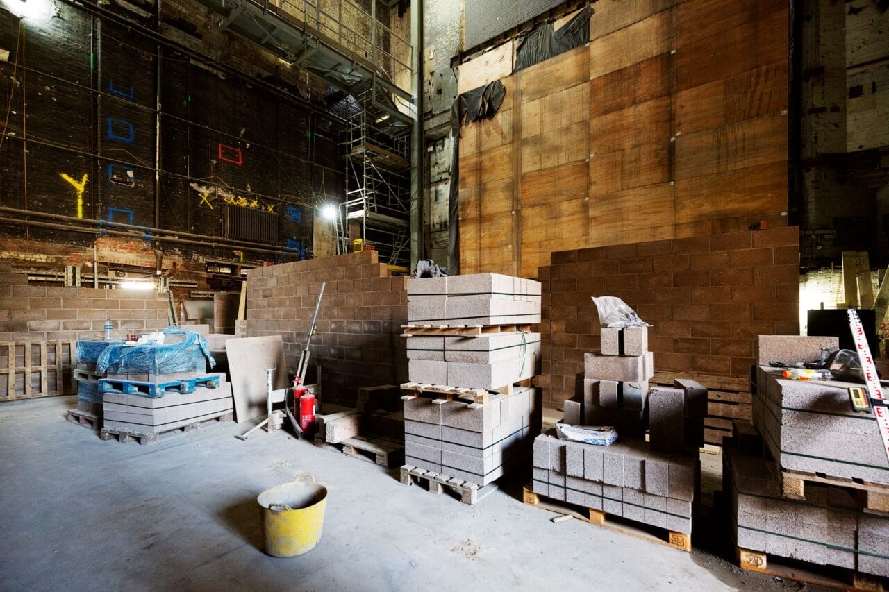 Stacks of concrete blocks and construction materials are arranged on pallets, in preparation for construction of the stage basement and stage floor in the King's Theatre.