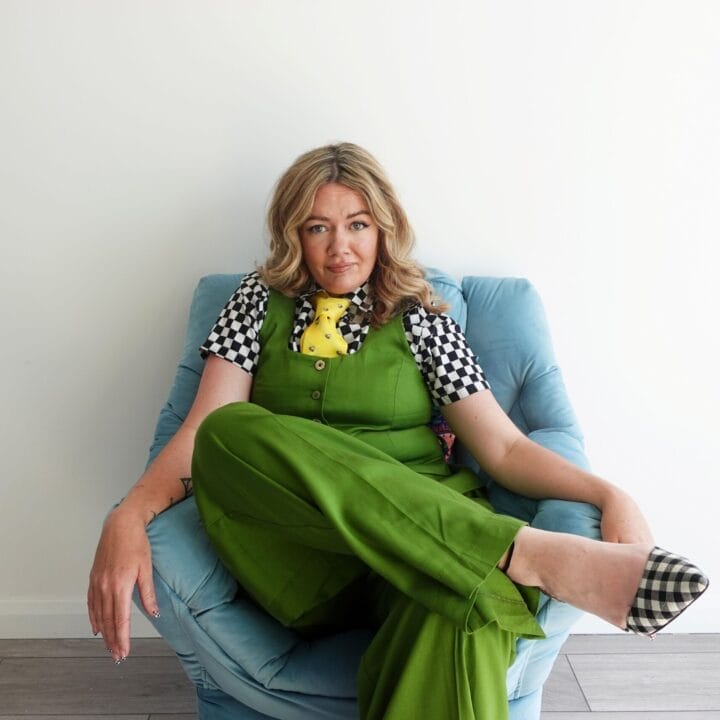 Person sitting in a blue chair against a white wall, wearing green pants, a checkered black-and-white top, and checkered shoes—capturing a serene therapy session reminiscent of Serena Terry’s calming style.