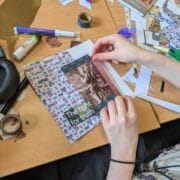A person assembles a collage on a desk, using patterned paper, cut-out images, and text reading "The fight for truth," surrounded by craft supplies and a leaflet from King's Theatre.