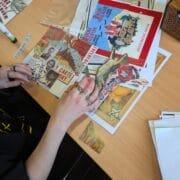 Person arranging vintage-style postcards, photos, and cut-out images on a desk, with glue sticks and other craft supplies, creating a collage inspired by King's Theatre.