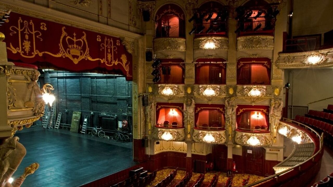 Interior of the Kings Theatre , featuring ornate balconies, red velvet seats, and an empty stage with the backstage area visible.