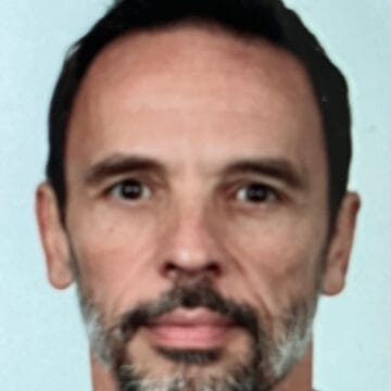 A man with short dark hair and a beard with some gray hairs, facing forward against a plain light background—Yvan Dubreuil.