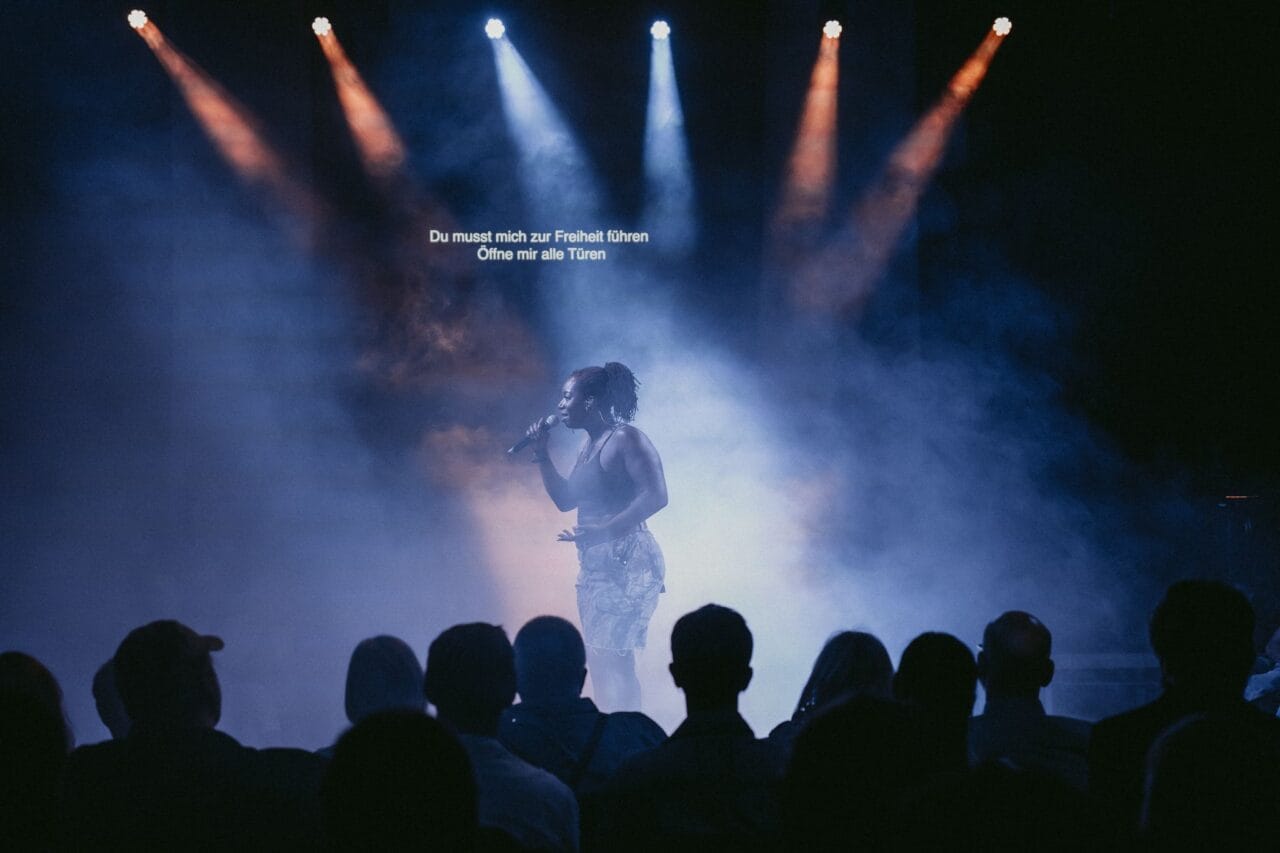 A singer performs on a smoky, dimly lit stage with spotlights, facing an audience—like a Half Man Half Bull confronting fate. German text appears above, reading: "Du musst mich zur Freiheit führen Ohne mit alle Trübn.