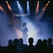 A singer performs on a smoky, dimly lit stage with spotlights, facing an audience—like a Half Man Half Bull confronting fate. German text appears above, reading: "Du musst mich zur Freiheit führen Ohne mit alle Trübn.