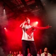 A person performs on stage with a microphone under red lights, channeling the energy of Half Man Half Bull, surrounded by an excited audience.