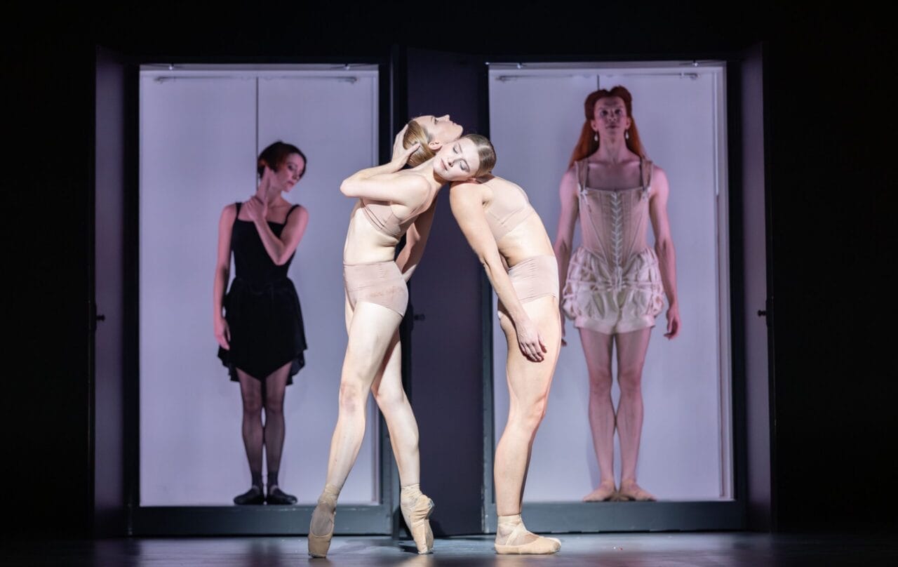 Four ballet dancers perform on stage, two posing back-to-back in the foreground, while two others evoke regal poise in separate doorways—a scene reminiscent of Mary, Queen of Scots’ elegant court.