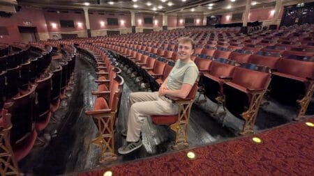 A person sits in the grand Festival Theatre, surrounded by rows of red seats and ornate armrests, enjoying exclusive access to the empty auditorium.