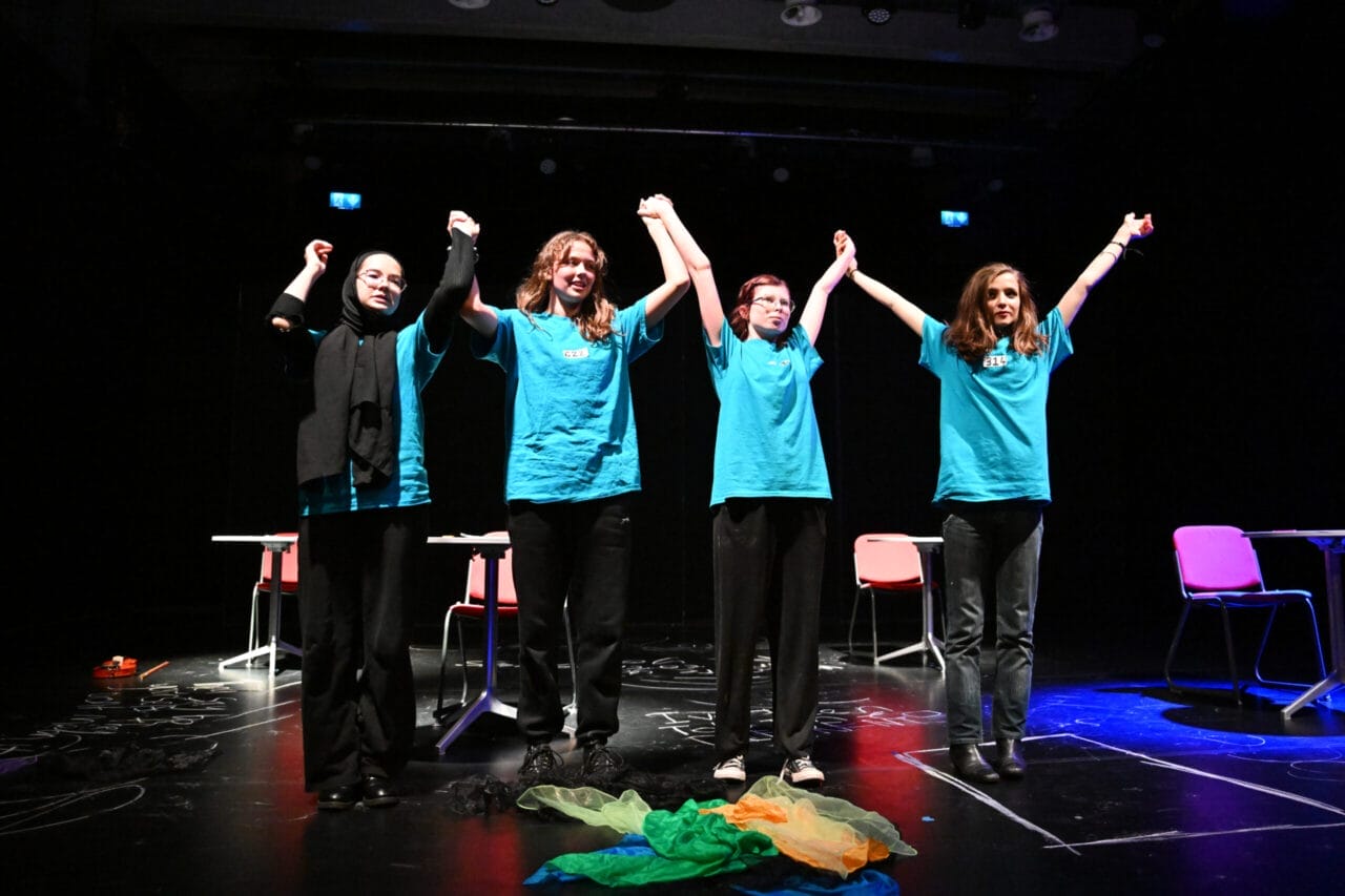 Four young people in light blue shirts stand, holding hands above their head readying themselves to bow.