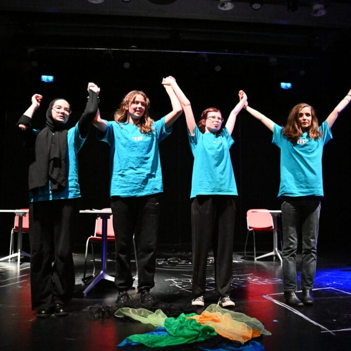 Four young people in light blue shirts stand, holding hands above their head readying themselves to bow.