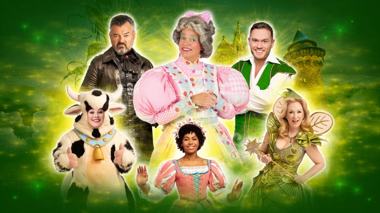 Six people in colorful fairy tale costumes, including a cow, stand in front of a glowing green background with a castle and clouds.