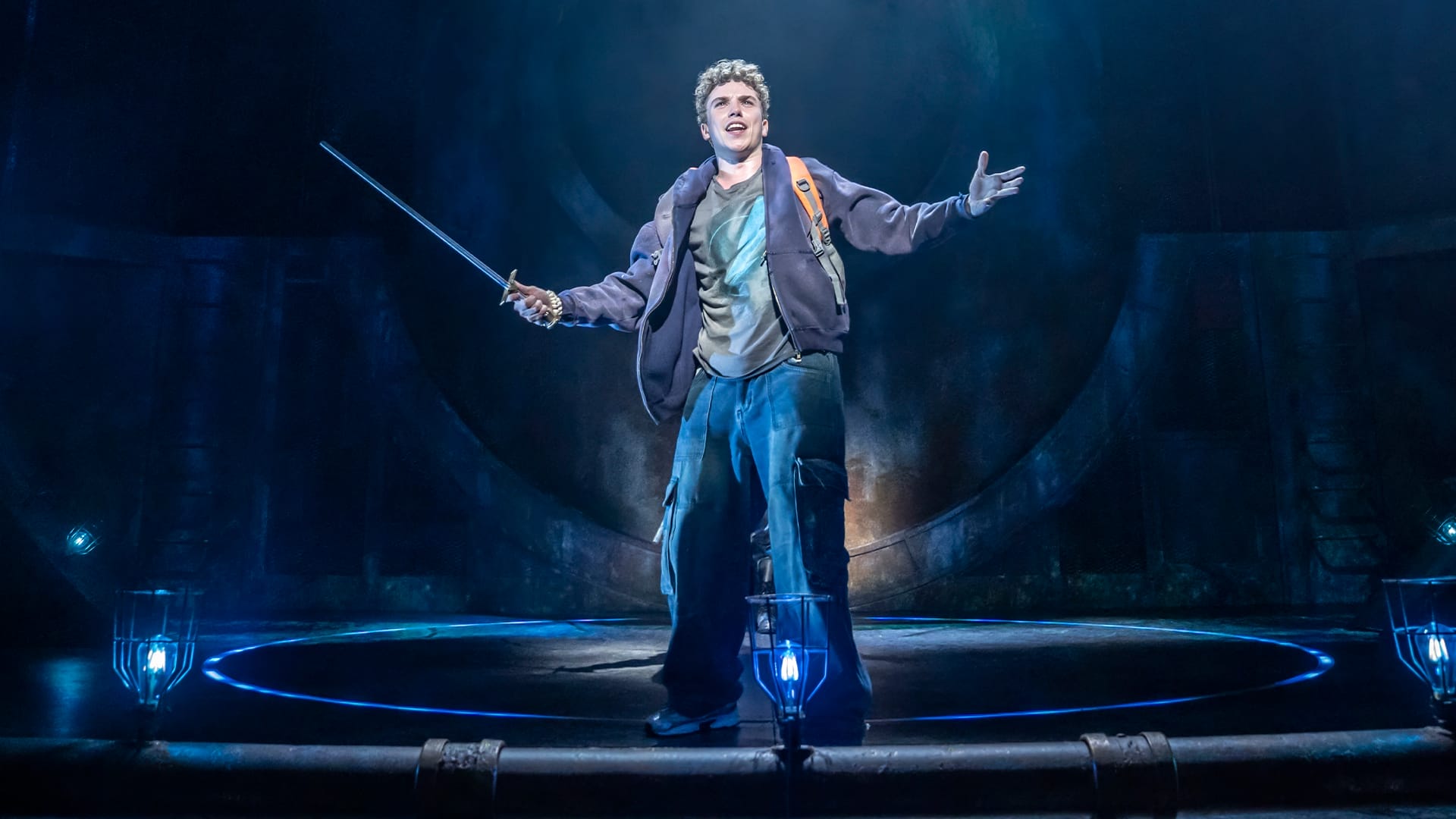 A man holding a sword stands center stage, as if ready to perform in a dramatic moment from musical theatre.