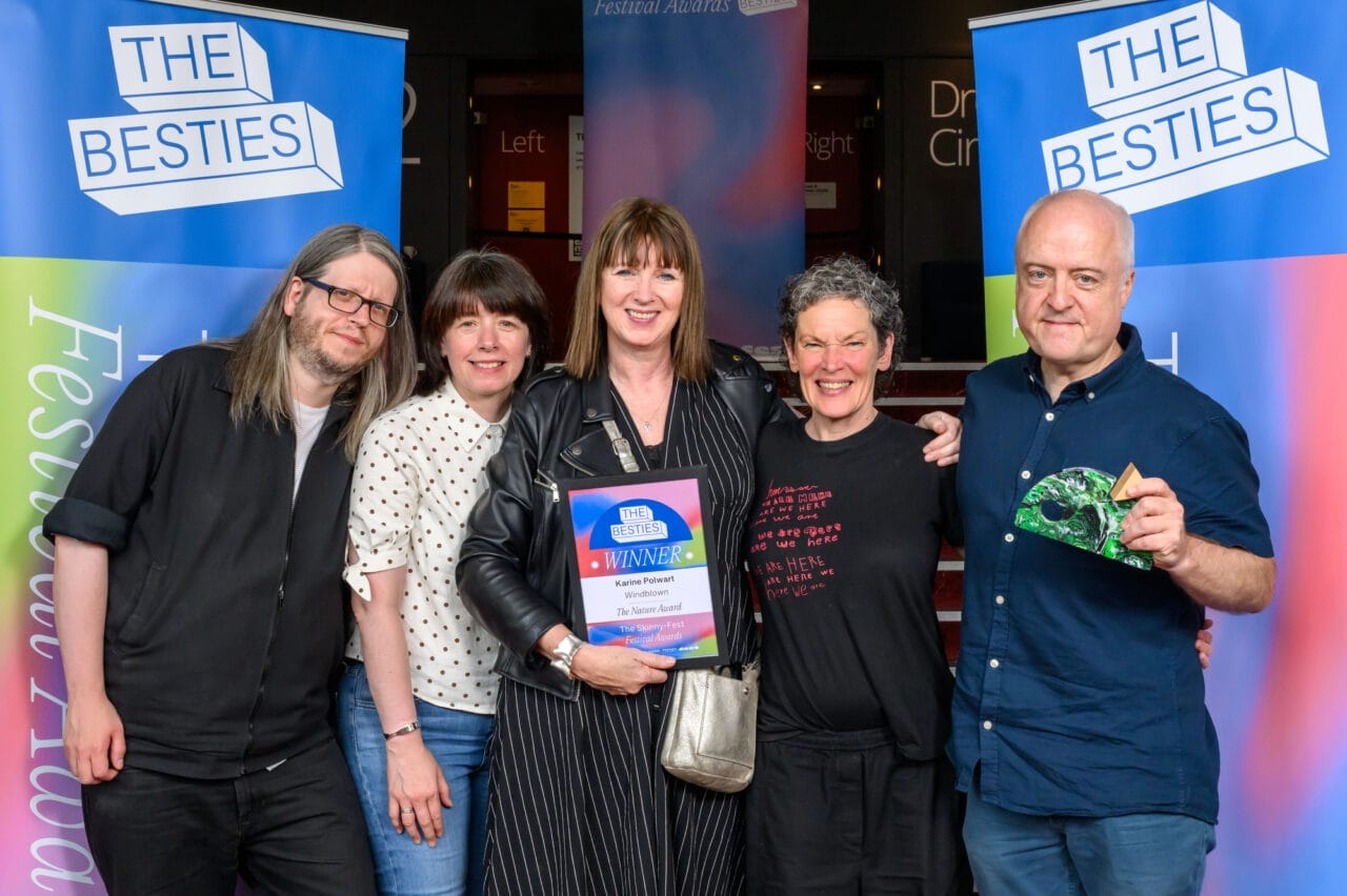 Five people stand together indoors at an awards event, with one person holding a winner’s certificate and another displaying a green, leaf-shaped trophy as the week two winners of the 2025 Besties.