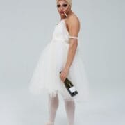A person in a white tutu, ballet shoes, and swim cap stands with a wine bottle and cigarette, channeling the playful spirit of Les Ballets Trockadero de Monte Carlo against a plain light background.