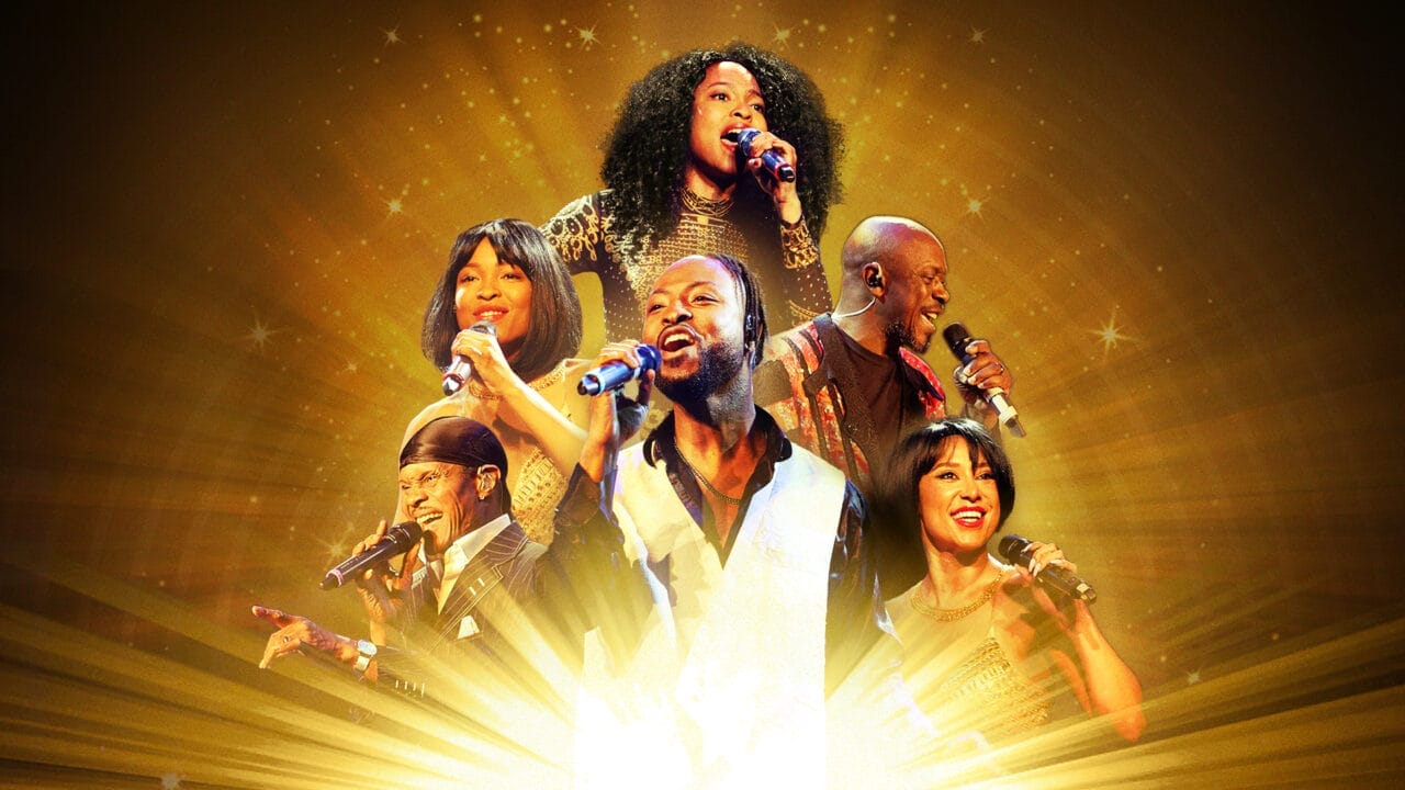 Six singers perform energetically on stage against a golden, radiant background, each holding a microphone and wearing formal or performance attire, bringing the Story of Soul to life with every note.