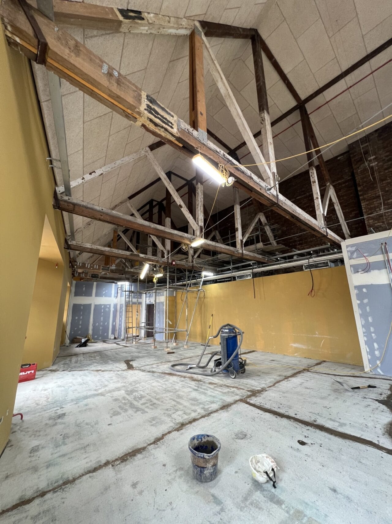 Interior of King’s Theatre Redevelopment under renovation, showcasing exposed beams, yellow walls, construction tools, scaffolding, and unfinished ceiling and floors.