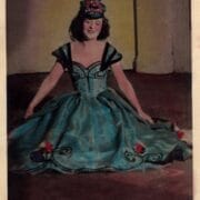 A woman in an off-the-shoulder gown with floral details and a matching headpiece sits on the floor against a plain background. A once black and white photo coloured in blue.