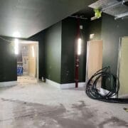 A partially constructed hallway in the King's Theatre Redevelopment, with exposed wiring, unfinished doorways, construction lights, a red pipe, and coiled cables on the floor.