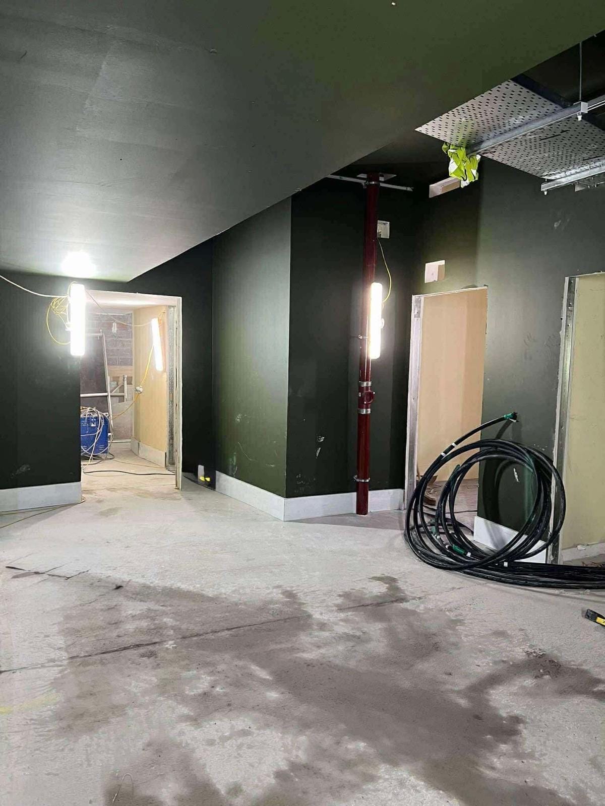 A partially constructed hallway in the King's Theatre Redevelopment, with exposed wiring, unfinished doorways, construction lights, a red pipe, and coiled cables on the floor.