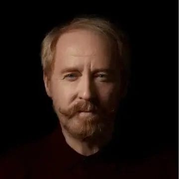 Headshot of Forbes Masson with the actor looking into camera, framed against a dark background.