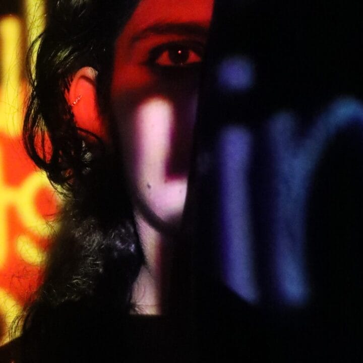 A person stands partially obscured in shadow with colorful, out-of-focus text projected onto their face and the background.