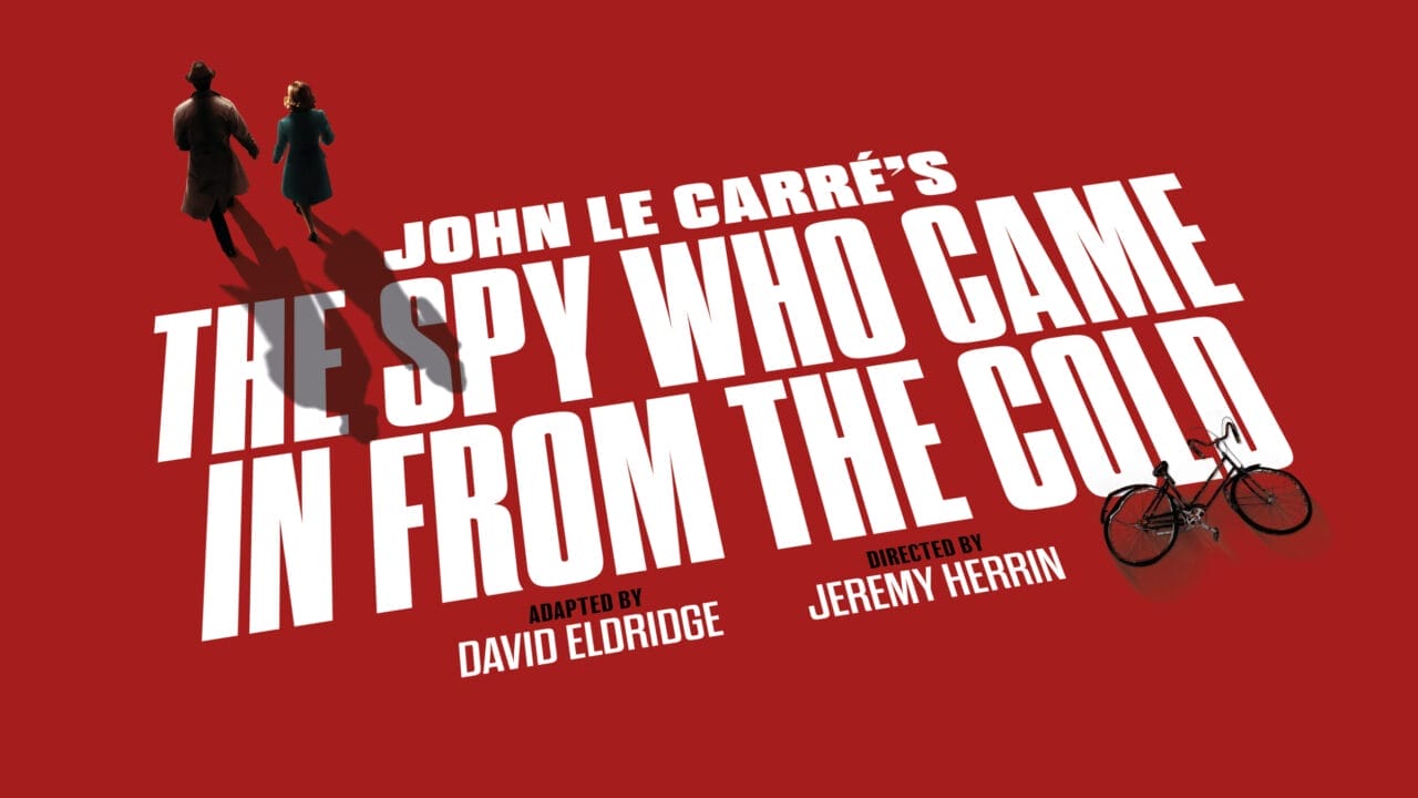 Red poster for "The Spy Who Came in from the Cold," the classic John le Carré spy novel, with two figures walking and a bicycle, featuring credits for David Eldridge and Jeremy Herrin.