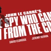 Red poster for "The Spy Who Came in from the Cold," the classic John le Carré spy novel, with two figures walking and a bicycle, featuring credits for David Eldridge and Jeremy Herrin.