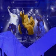 Three people pose in hip hop rap posture, hands in the air, over a blue background with Scottish saltire flag spray painted like graffiti