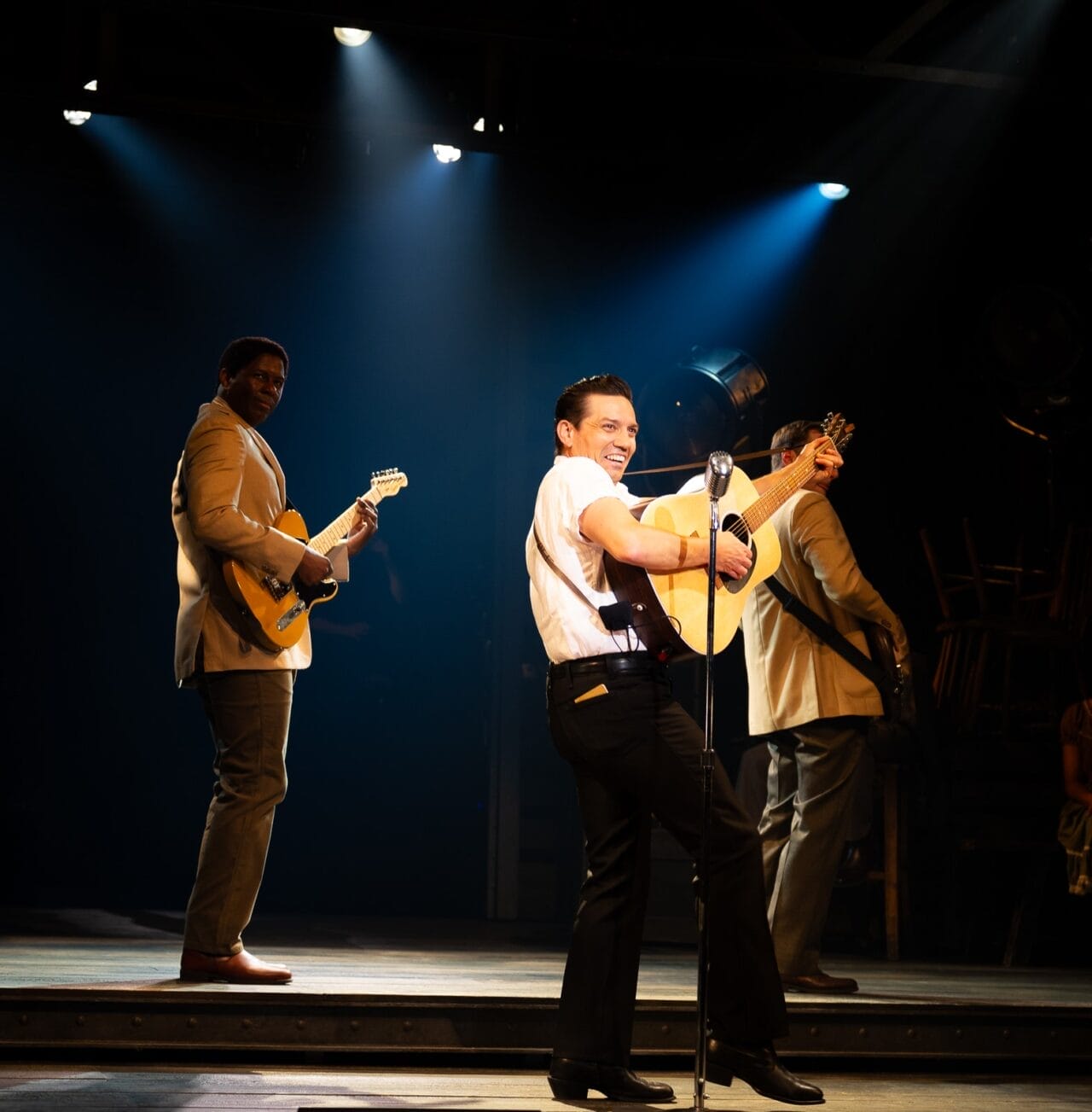 Man in white shirtsleeves singing on stage with big guitar
